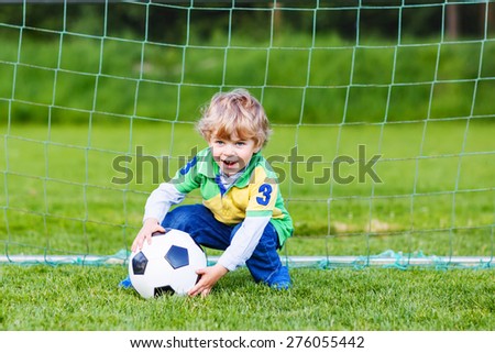 Active cute little toddler playing soccer and football and having fun, outdoors on field. Active leisure with children on warm sunny summer day.
