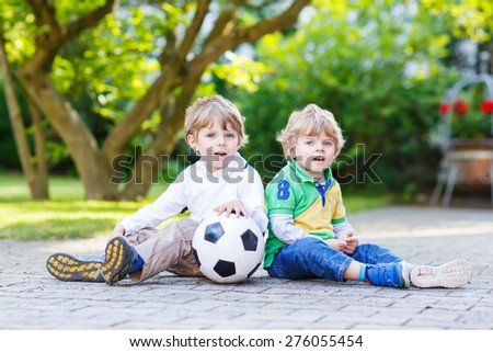 Two active twins playing soccer and football and having fun, outdoors. Active leisure with children on warm sunny summer day.