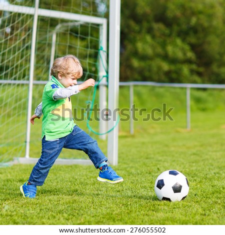 Active cute little kid boy playing soccer and football and having fun, outdoors on field. Active leisure with children on warm sunny summer day.