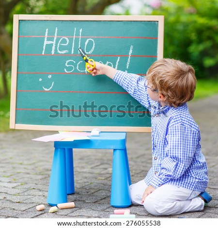 Happy adorable little kid boy with glasses at blackboard practicing writing, outdoor. school or nursery. Back to school concept