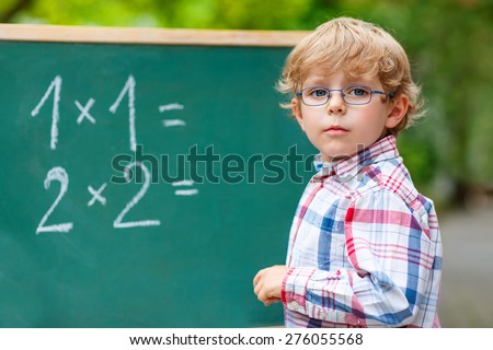 Adorable preschool kid boy with glasses at blackboard practicing mathematics, outdoor. school or nursery. Back to school concept