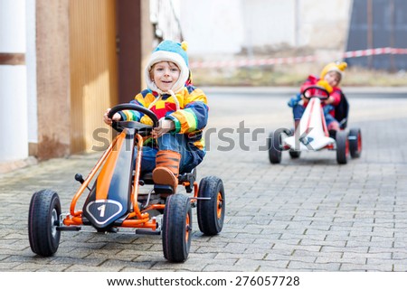 Two funny little kids and sibling boys having fun with toy race cars, outdoors. Friends having a competition. Outdoor games for children concept.