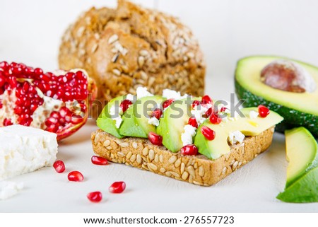 Avocado with Feta, pomegranate and olive oil on sunflower seeds bread sandwich. Healthy organic and vegan breakfast, on white wooden background