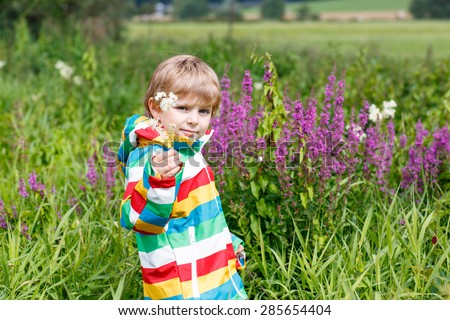 Little blond boy with lot of wild flowers on sunny summer day. Happy child enjyoing nature.