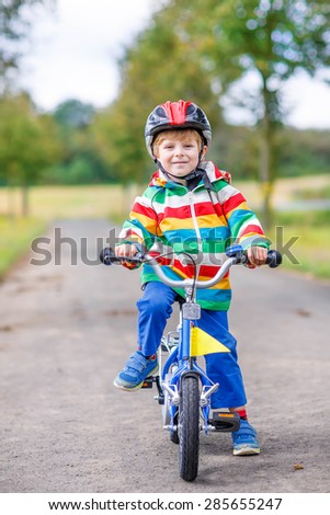 Happy adorable kid boy in safety helmet and colorful clothes on bike on summer day. Active leisure for children outdoors.