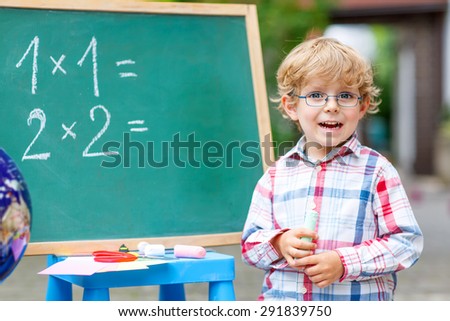 Happy funny little kid boy with glasses at blackboard practicing mathematics, outdoor. school or nursery. Back to school concept