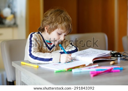 Portrait of cute happy preschool kid boy at home making homework. Little child painting with colorful pencils, indoors.