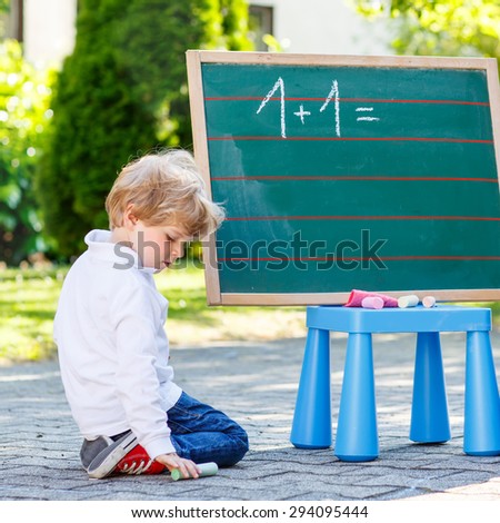 Two sibling boys at blackboard practicing mathematics, outdoor school or nursery. Kid learning and schoolboy concept. On summer sunny day. Back to school.