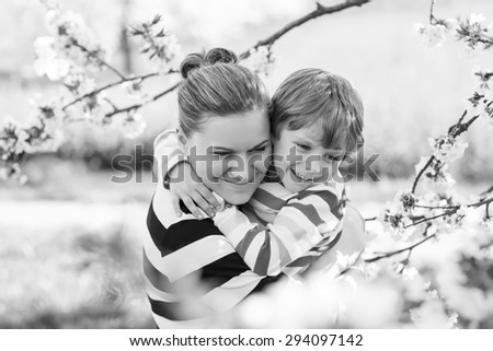 Little cute boy and young mum hugging in blooming cherry garden in spring. Happy family celebrating mother\'s day.