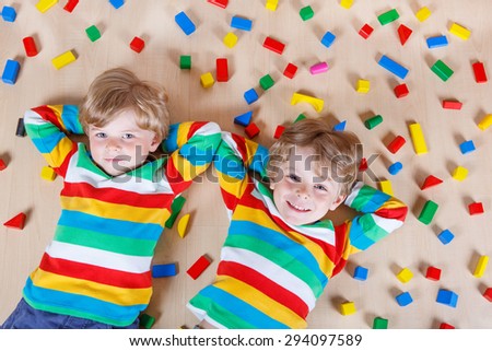 Two little blond children playing with lots of colorful wooden blocks indoor. Active kid boy wearing colorful shirt and having fun with building and creating.