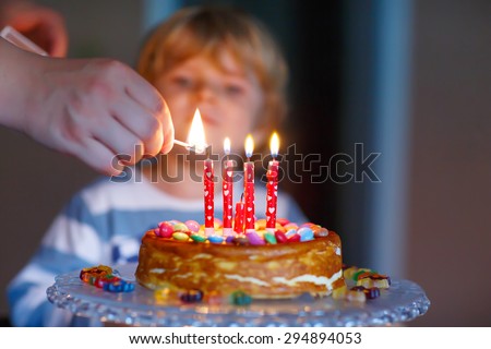 Adorable four year old kid celebrating his birthday and blowing candles on homemade baked cake, indoor. Birthday party for kids. Hand of adult with match