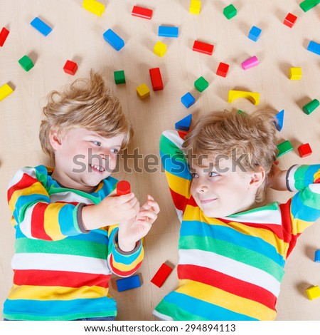 Two little blond friends playing with lots of colorful wooden blocks indoor. Active kid boy wearing colorful shirt and having fun with building and creating.