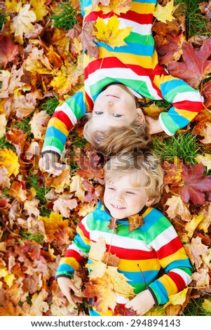 Two blond boys lying in autumn leaves in colorful clothing. Happy siblings having fun in autumn park on warm day.