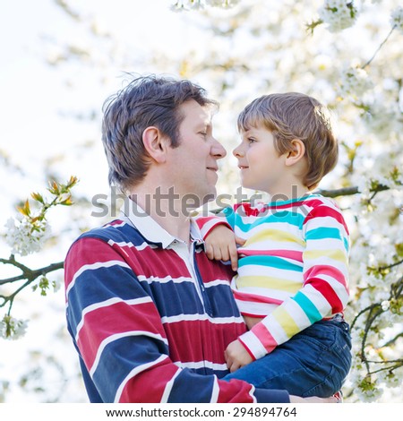 Happy little kid boy and his dad in blooming cherry garden in spring. Happy family celebrating father\'s day.