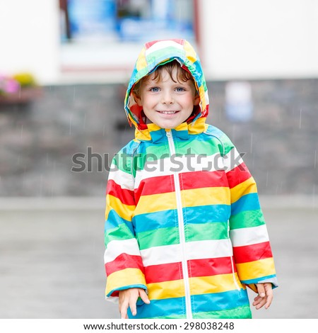 Happy cute little child walking through rain in waterproof jacket. Kid having fun on rainy day.