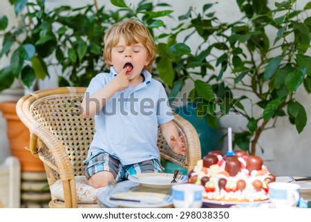 Funny cute boy celebrating his third birthday in home's garden with big cake. Happy child laughing about gifts and tasting cake. Outdoors on sunny day.