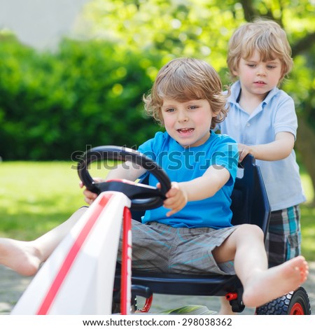 Two funny little boy friends having fun with toy race car in summer garden, outdoors. Active kid pushing the car with younger boy. Outdoor games for children in summer concept.