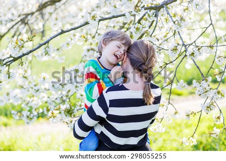 Happy little boy and his mother hugging in blooming cherry garden in spring. Happy family celebrating mother\'s day.