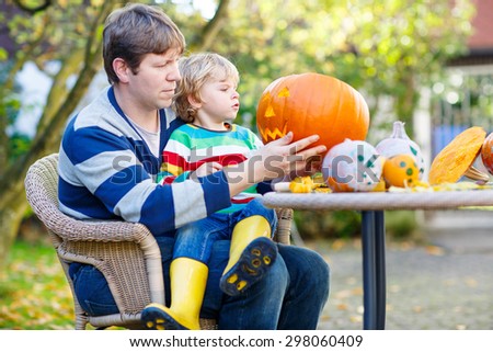 Adorable little child and his father carving jack-o-lantern for halloween in autumn garden, outdoors. Family having fun together and celebrating thanksgiving.