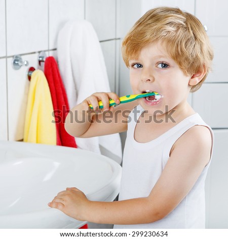 Little blond boy learning brushing his teeth in domestic bath. Kid learning how to stay healthy. Health care concept.