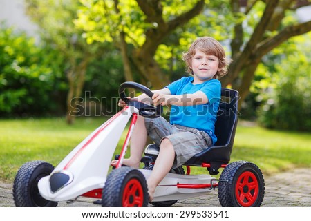 Funny happy  little kid boy having fun and driving toy race car in home\'s garden. Active games for children in summer. On warm sunny day.