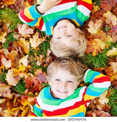 Two happy children lying in autumn leaves in colorful clothing. Happy siblings having fun in autumn park on warm day.