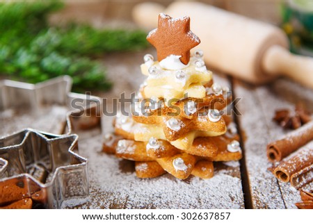 Homemade baked Christmas gingerbread tree on vintage wooden background. Anise, cinnamon, baking roll, star forms and decoration utensils. With icing sugar snow. Selfmade gift for xmas.