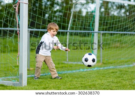 Active cute little kid boy playing soccer and football and having fun, outdoors on field. Active leisure with children on warm sunny summer day.