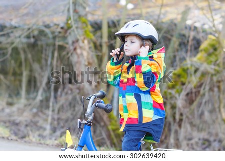 Little kid boy wearing safety helmet and riding his first bike and having fun on cold  day, outdoors. Active leisure with children in winter, spring or autumn.
