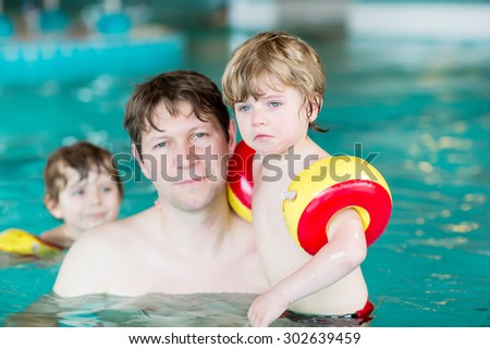 Two little kid boys and their dad in swimming pool.  kid boys, siblings and twins wearing safe swimmies. One boy crying