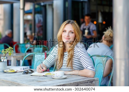 Young beautiful woman drinking coffee and writing diary, book or notes in an outdoor cafe in Paris, France.