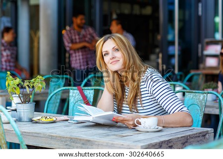 Young beautiful woman drinking coffee and reading book in an outdoor cafe in Hamburg, Germany.