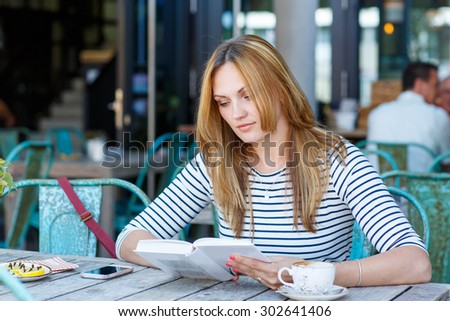 Young beautiful girl drinking coffee and reading book in an outdoor cafe in Munich, Germany