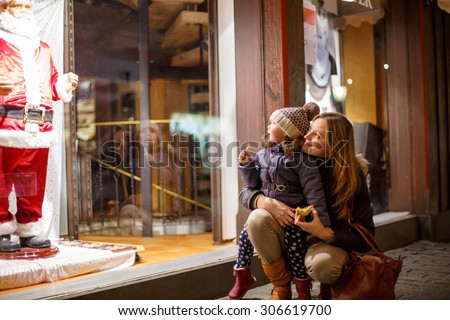 Little toddler girl with mother on Christmas market. Funny happy kid making window shopping with  Santa Claus. holidays, christmas, childhood and people concept