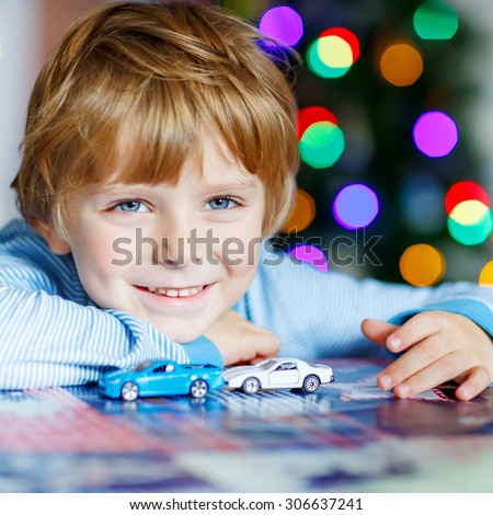 Adorable kid boy playing with cars and toys at home, indoor. funny child having fun with gifts. Colorful christmas lights on background. Family, holiday, kids lifestyle concept.