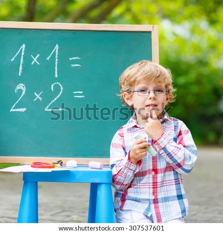 Cute little kid boy with glasses at blackboard practicing mathematics, outdoor. school or nursery. Back to school concept