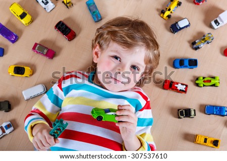 Adorable cute child with lot of different colorful toy cars. Happy boy playing with toys at nursery. People, Lifestyle, Family concept.