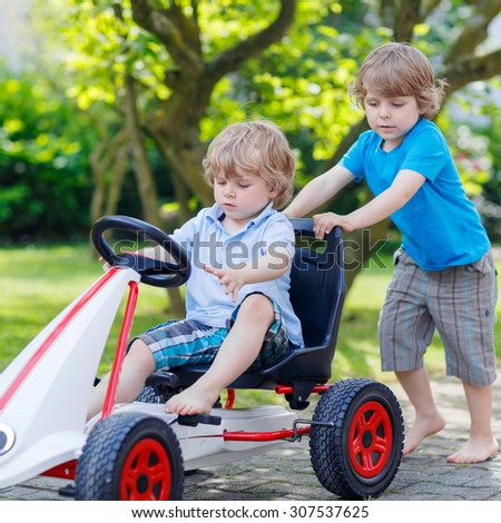 Two happy active little kid and sibling boys having fun with toy race car in summer garden, outdoors. Adorable brother pushing the car with younger child. Outdoor games for children in summer concept.