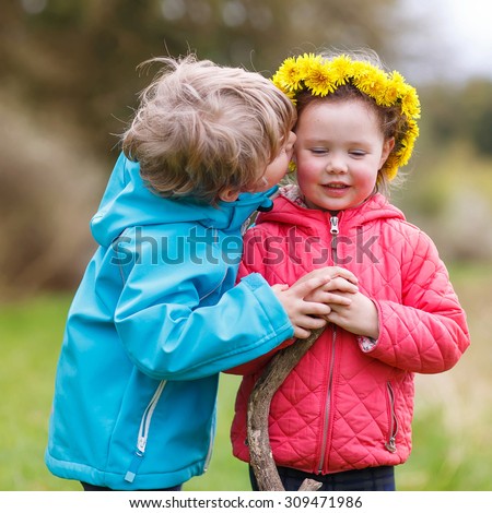 Two little cute smiling kids in bright jackets hugging in a forest on a rainy day. Friendship between siblings. Happy family concept