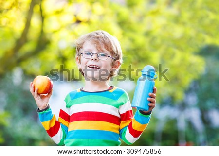 Beautiful little kid boy with  apple and drink bottle on his first day to elementary school or nursery. Outdoors.  Back to school, kids, lifestyle concept