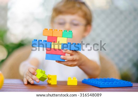Little child with glasses playing with lots of colorful plastic blocks indoor. kid boy having fun with building and creating. Selective focus on toy