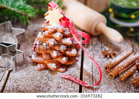 Homemade baked Christmas gingerbread tree on vintage wooden background. Anise, cinnamon, baking roll, star forms and decoration utensils. With icing sugar as snow. Selfmade gift for xmas.