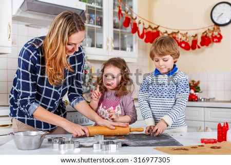 Happy family baking Christmas cookies at home. Woman, little son and daughter having fun in domestic decorated kitchen. Traditional leisure with kids on Xmas