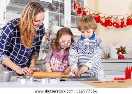 Happy family baking Christmas cookies at home. Little brother, sister and mother having fun in domestic decorated kitchen. Traditional leisure with kids on Xmas