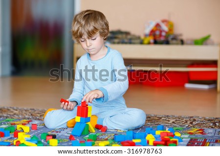 Adorable little child playing with lots of colorful wooden blocks indoor. Active kid boy  having fun with building and creating. People, lifestyle, childhood, nursery concept