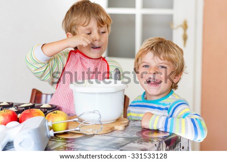 Two little funny brothers baking apple cake in domestic kitchen. Kid boys having fun with working with mixer, eggs and fruits. Children tasting dough