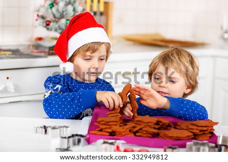 Two adorable little friends baking gingerbread cookies. Happy kid boys, children in blue xmas pullovers. Playing and having fun. Kitchen decorated for Christmas. Family, holiday, kids lifestyle