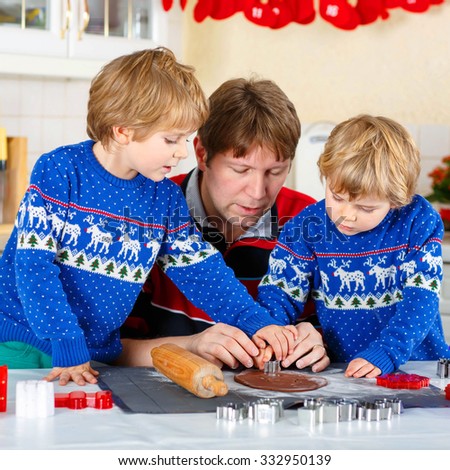 Two little siblings and father baking gingerbread cookies. Happy siblings, children in blue xmas pullovers. Kitchen decorated for Christmas. Family, holiday, kids lifestyle concept.