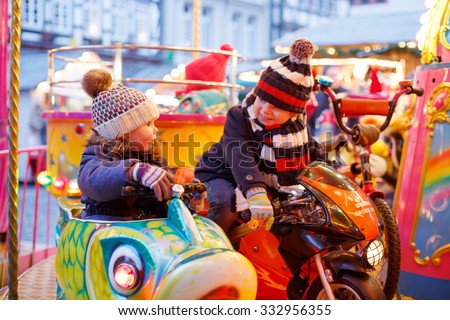 Adorable little boy and girl, siblings on a carousel at Christmas funfair or market, outdoors. Happy children, friends having fun. Selective focus on one child. Holiday, children, lifestyle concept.