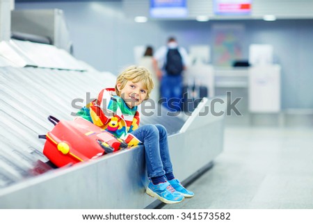 Beautiful little tired kid boy at the airport, traveling. Happy child waiting with kids suitcase on baggage carousel. Canceled flight due to pilot strike.